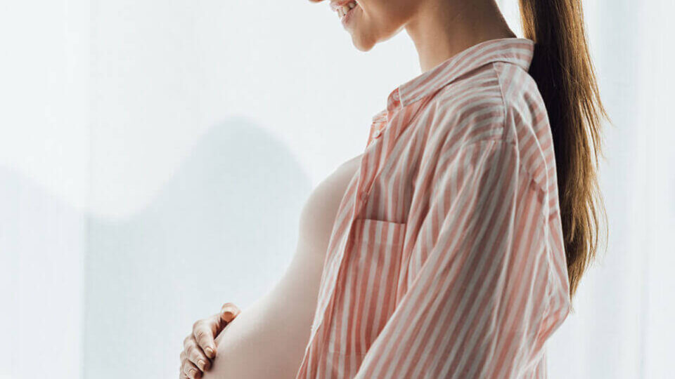 side view of happy pregnant woman smiling and touching belly