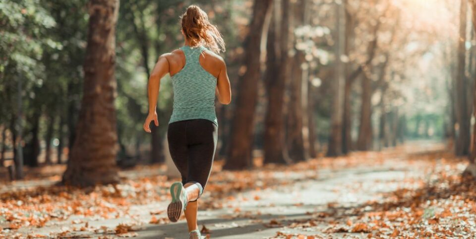 Frau joggt auf einem mit Herbstblättern bedeckten Weg in einem sonnigen Park.