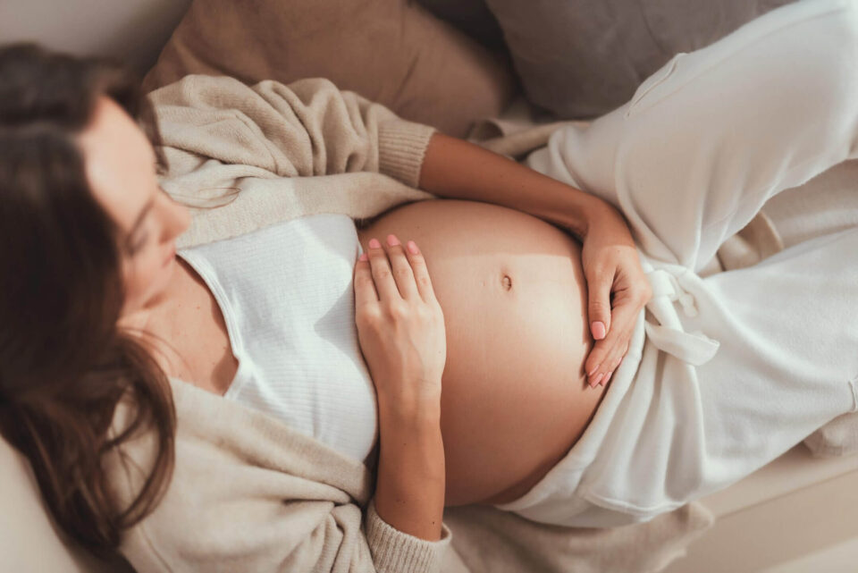 Schwangere Frau formt mit ihren Händen ein Herz über ihrem Babybauch – Symbol für Liebe und Vorfreude auf die Geburt.