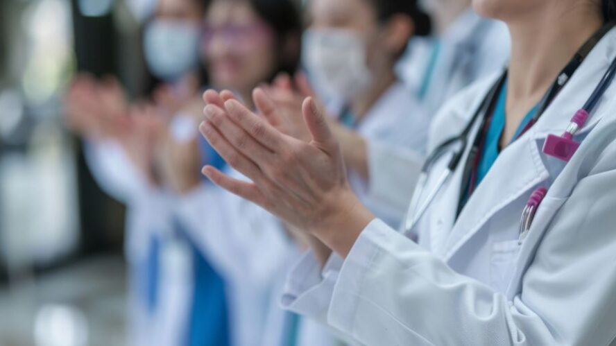 Gruppe von Ärzten und medizinischem Fachpersonal klatscht, symbolisch für Teamarbeit und Anerkennung im Gesundheitswesen.