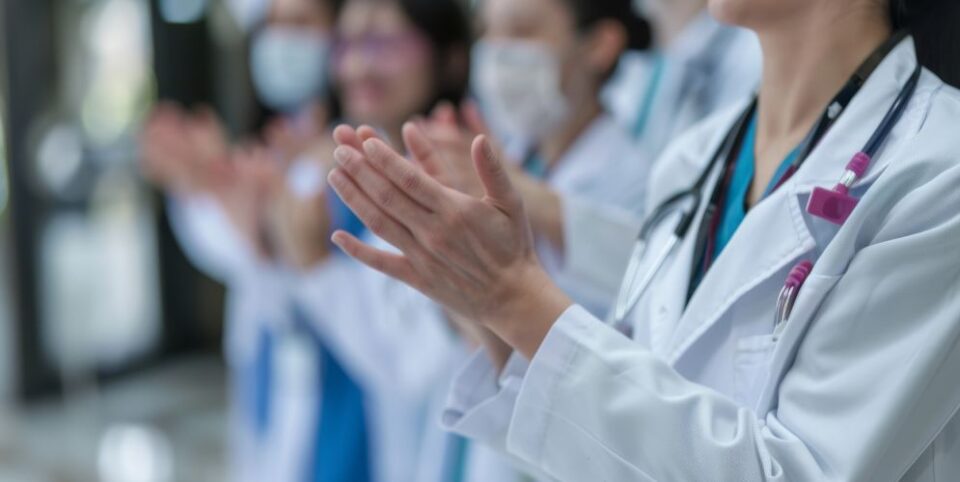 Gruppe von Ärzten und medizinischem Fachpersonal klatscht, symbolisch für Teamarbeit und Anerkennung im Gesundheitswesen.