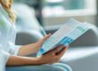 Frau sitzt in einem modernen Wartezimmer und liest eine Broschüre oder ein Informationsblatt – Fokus auf Gesundheits- oder Bildungsthemen.