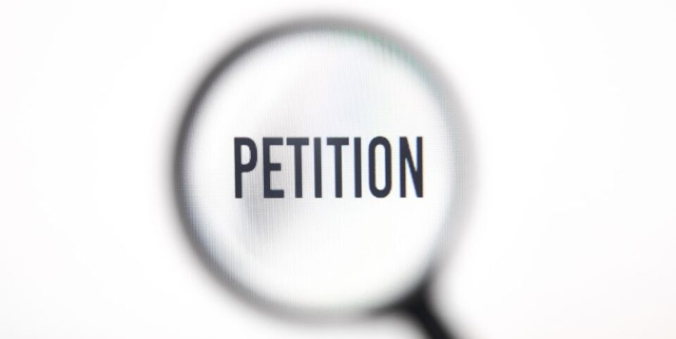 Das Wort 'Petition' erscheint vergrößert durch eine Lupe auf weißem Hintergrund – Fokus auf rechtliche oder gesellschaftliche Anliegen