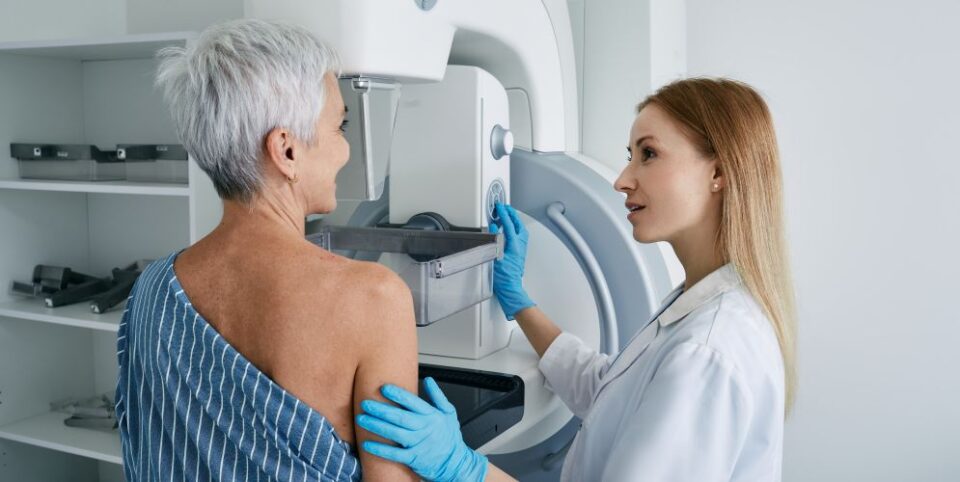 Ärztin unterstützt eine ältere Frau bei einer Mammographie-Untersuchung an einem modernen Gerät – Fokus auf Brustkrebsvorsorge und medizinische Betreuung.