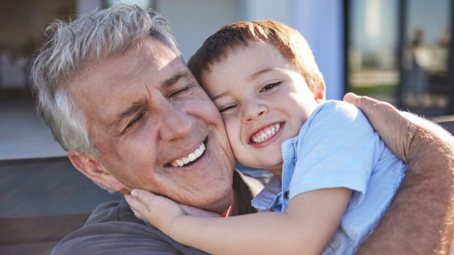 Lächelnder Großvater umarmt seinen Enkelkind, beide wirken glücklich und entspannt im Freien – Fokus auf Familie und generationsübergreifende Beziehungen