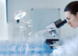 Wissenschaftlerin im Labor untersucht eine Probe unter einem Mikroskop, umgeben von Laborgeräten – Fokus auf Forschung und Analyse.
