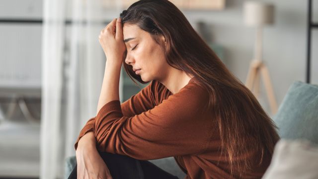Frau sitzt nachdenklich auf einem Sofa, symbolisiert postpartale Depression.